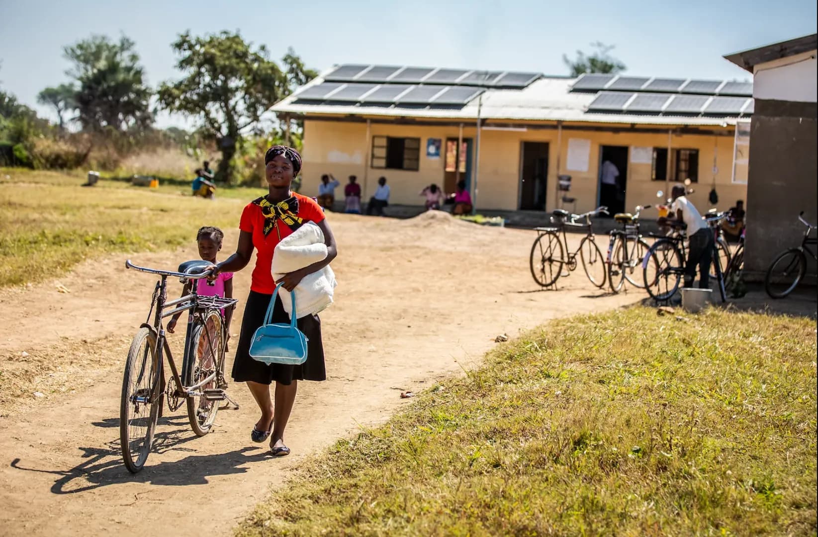 Mother and child walking past a rural health facility with solar panels on its roof