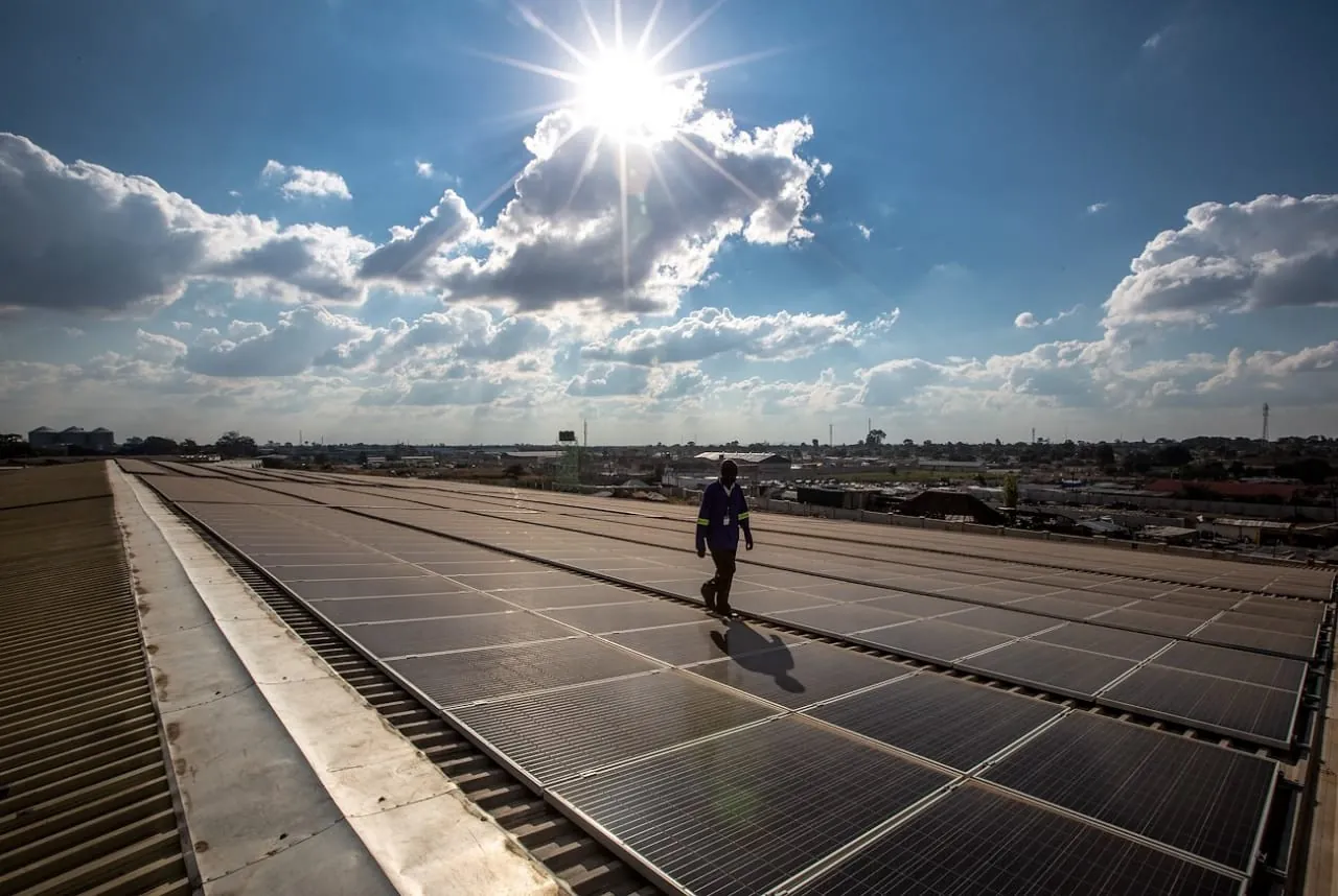 Technician walking across a large rooftop solar array under a bright sky