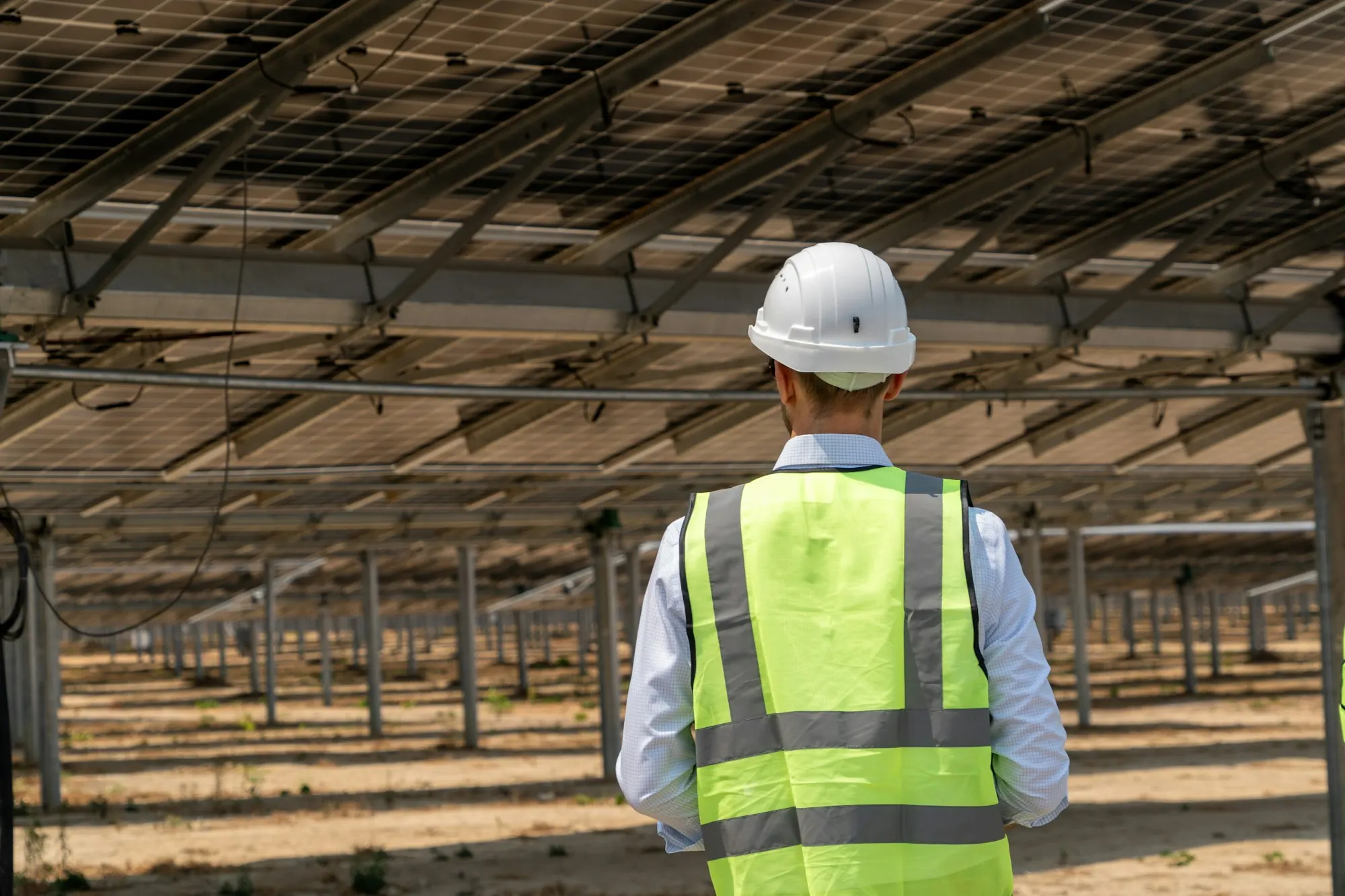 Engineer in a hard hat inspecting ground-mounted solar panels