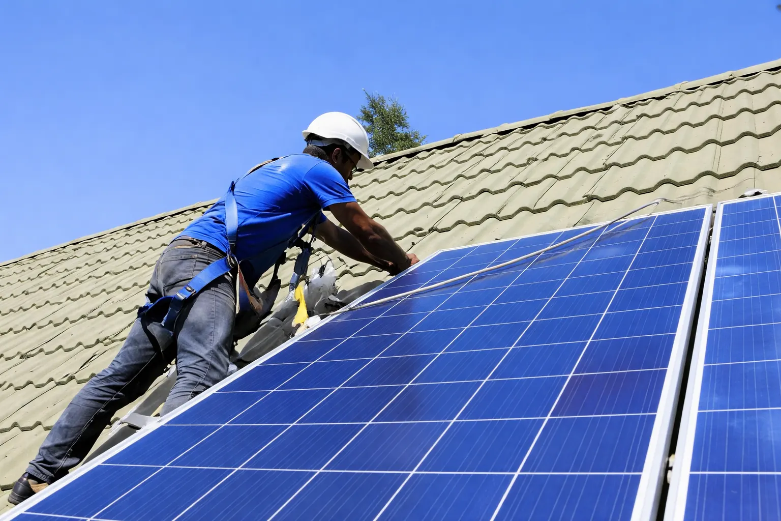 Solar technician in a hard hat mounting panels on a tiled roof